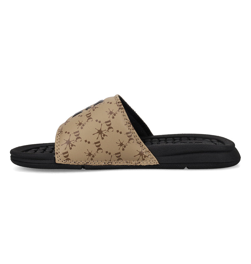 The Kids' Bolsa Slides by DC Shoes feature a tan patterned upper with abstract brown designs and a black cushioned sole, displayed in profile against a white background—ideal for kids seeking stylish and comfy sandals.