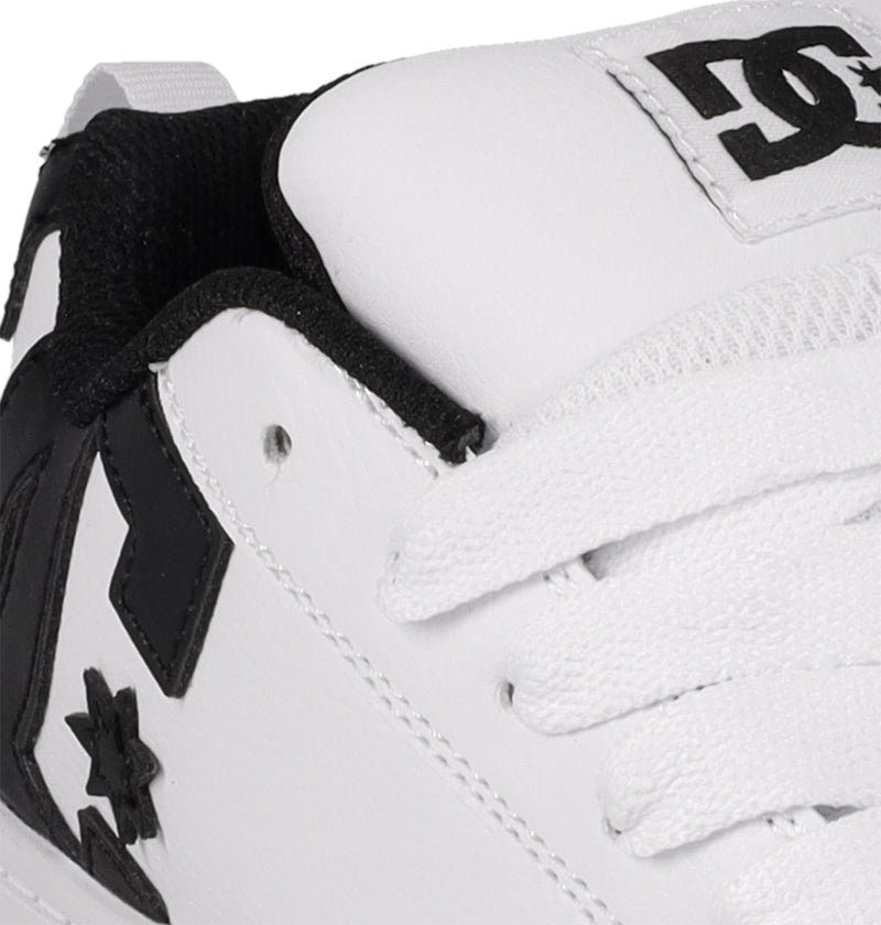 Close-up of DC Shoes Kids' Court Graffik: a white sneaker with black accents, visible stitching, white laces, black inner lining, and DC logos by the laces and heel. Skate-inspired style from DC Shoes.