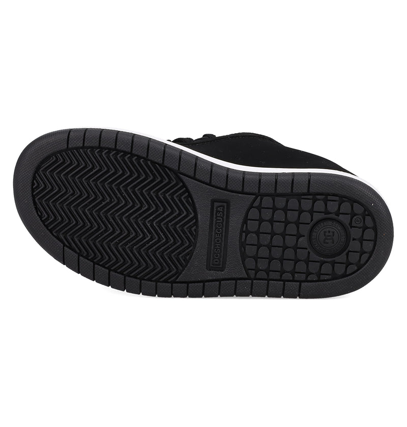 The image shows the black rubber sole of DC Shoes Kids' Court Graffik, featuring a circular DC logo, rectangular textured area, and herringbone tread for grip. Part of the shoe’s classic puffy black silhouette is also visible.