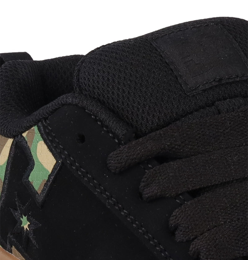Close-up of DC Shoes Kids' Court Graffik, a puffy black sneaker with black laces, mesh tongue with stitched DC logo, and camouflage star detail on the side.
