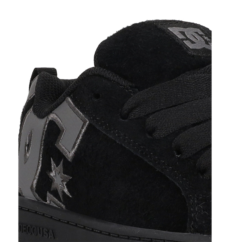 Close-up of the Kids' Court Graffik Special Edition Shoes by DC Shoes—a black sneaker with black laces, shiny silver accents, a star design, and the DC Shoes logo on the side and tongue.