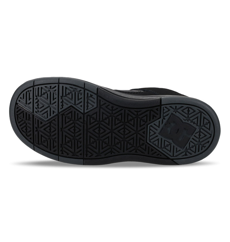 The image shows the black rubber sole of the Kids' DC Shoes Cure Elastic Shoes by DC Shoes, featuring a geometric tread pattern, segmented areas for flexibility, and a stylized DC logo embossed near the heel.