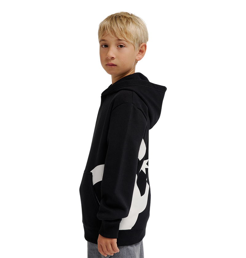 A young boy with blond hair wears the DC Shoes Lanai Hoodie Youth, a black pullover with bold side graphics, standing sideways and looking at the camera against a plain white background.