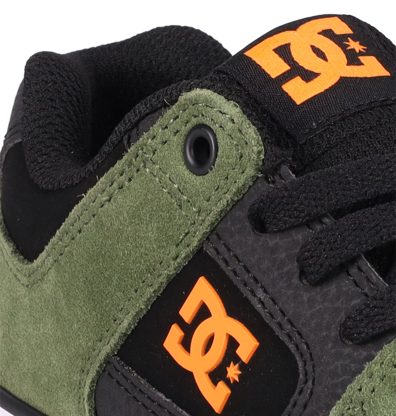 Close-up of DC Shoes Kids' Pure Shoes featuring green suede sides, black laces, and bright orange DC logos on the tongue and side. Black and green details with a textured pattern create a comfortable, stylish look for kids.