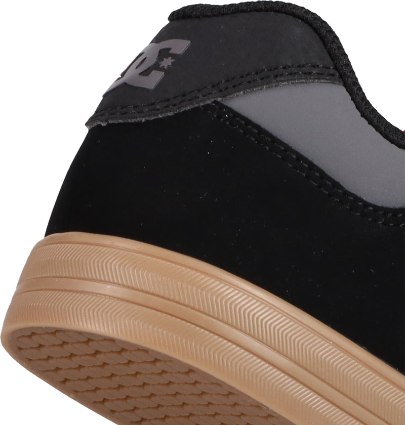 Close-up of the heel of black and gray DC Shoes Kids' Pure Shoes with a tan rubber sole and textured tread. The back features a DC logo with star on the heel tab, blending style and comfort for kids.