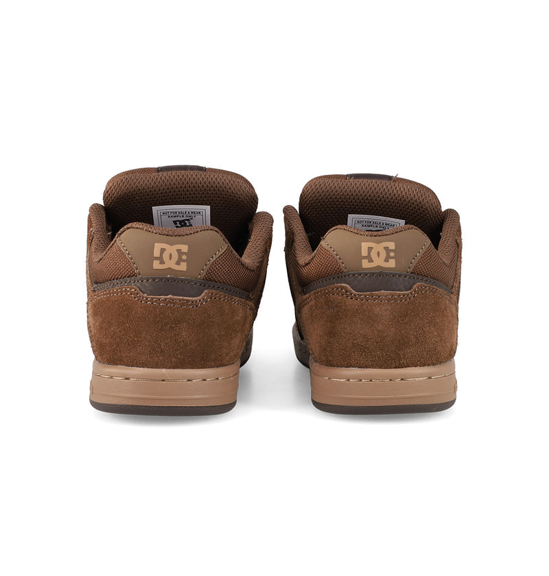 A pair of Kids' Stag Shoes by DC Shoes in brown suede, seen from the back with DC logos on the heels and padded collars. They have brown midsoles, dark outsoles, and a classic cupsole design for authentic skate style.