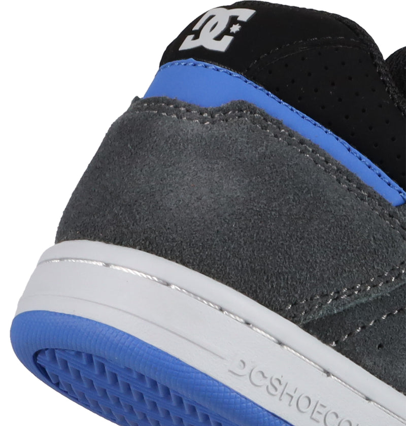 Close-up of the heel on DC Shoes' Kids' Stag Shoes showing grey suede, blue and black accents, white stitching, and a black heel tab with the DC logo. Features cupsole construction with a blue outsole and crisp white midsole.