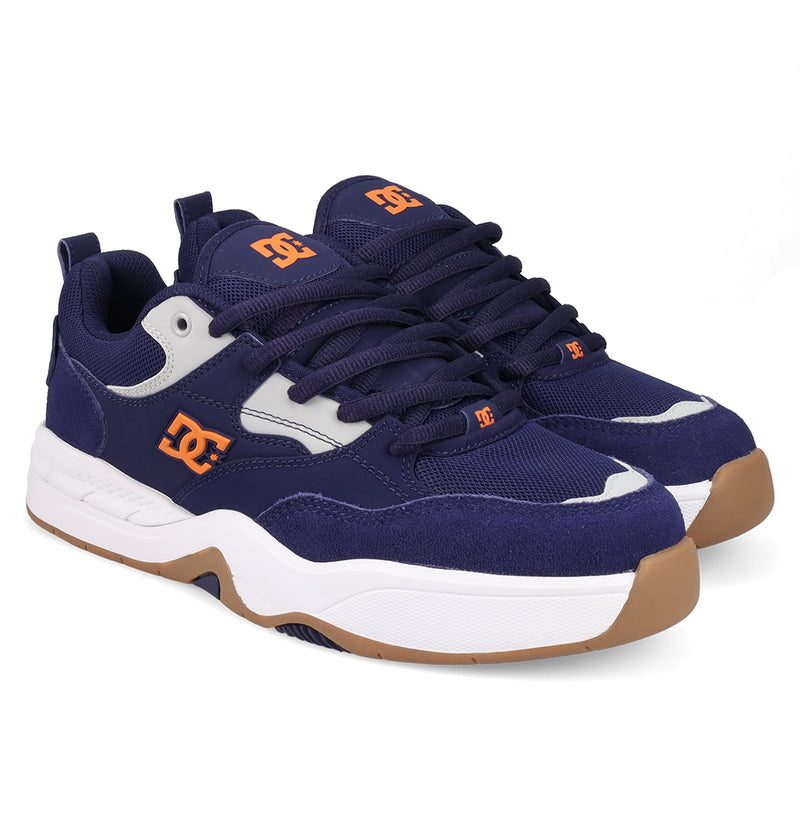 The Men's DC Ascend S Shoes by DC Shoes feature a navy blue upper with white and tan accents, orange DC logos, white midsoles, gum outsoles, and dark blue laces for classic style and modern comfort—displayed on a white background.