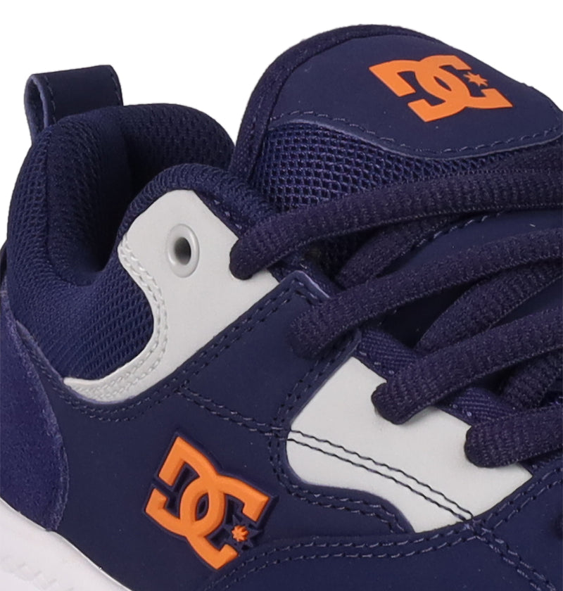 Close-up of the Men's DC Ascend S Shoes by DC Shoes in navy blue with white accents and an orange logo, featuring dark blue laces, breathable mesh details, and modern comfort inspired by classic DC style.