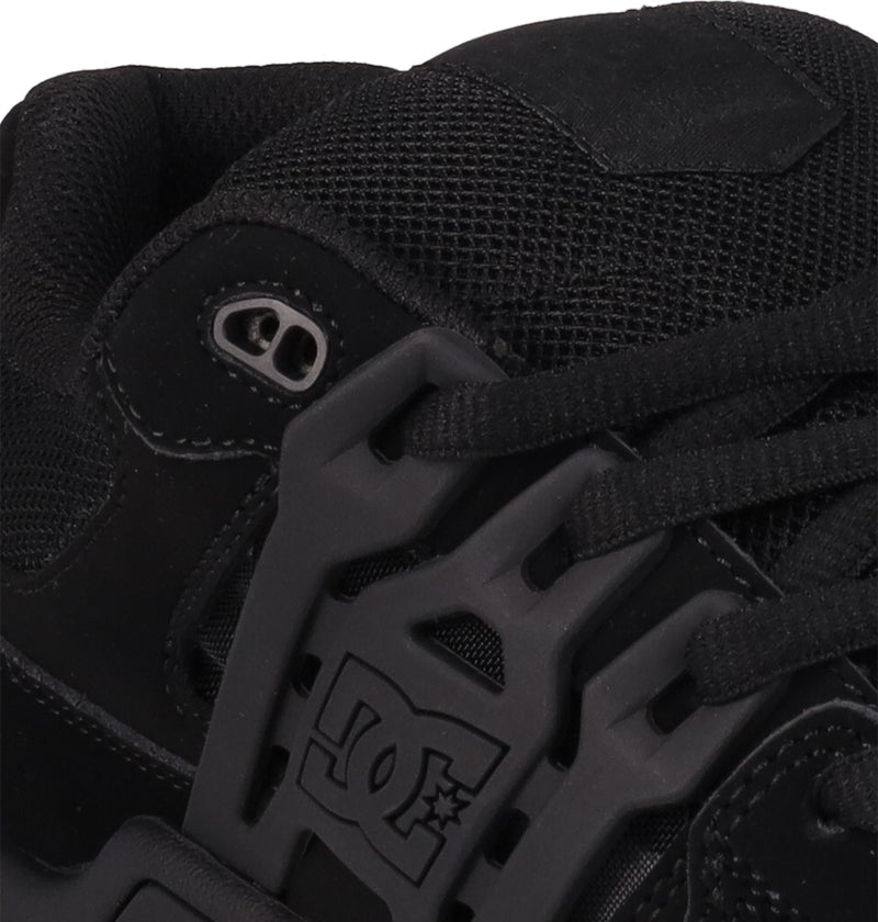 Close-up of DC Shoes Men's AT-2 skate shoe in black, featuring detailed stitching, black laces with metal eyelets, a DC Shoes logo on the plastic lace guard, and an Airband outsole.
