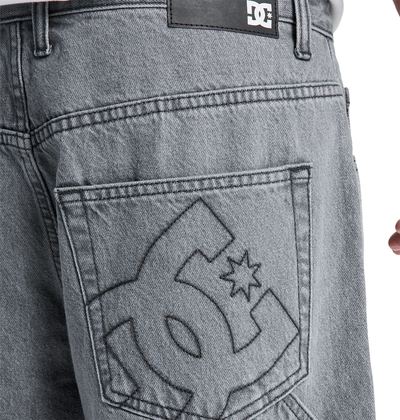 Close-up of the back pocket on DC Shoes Men's Baggy Denim Carpenter Pant in gray heavyweight denim, featuring a large embroidered logo and a black leather brand patch above the pocket, highlighting its wide-leg fit.