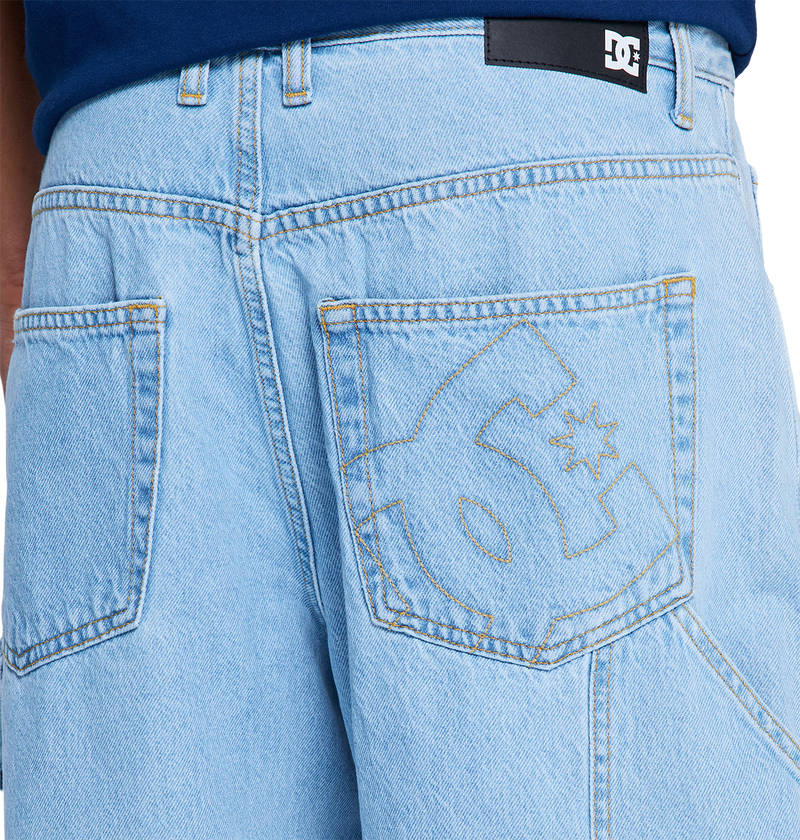 Close-up of DC Shoes Men's Baggy Denim Carpenter Pant in light blue heavyweight denim, featuring a large stitched DC Shoes logo on the back pocket, black label on waistband, and a bold wide-leg fit.