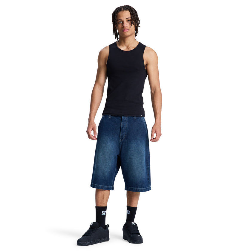 A young man faces forward wearing a Reebok black tank top, Baggy Denim Jort shorts, black socks, and black sneakers against a plain white background.