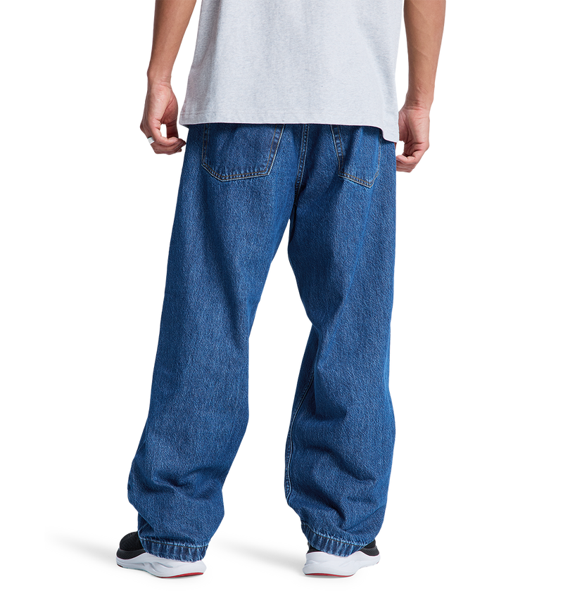 A person wearing a white t-shirt, DC Shoes Men's Baggy Denim Pant, and black and white sneakers stands with their back to the camera against a plain white background.