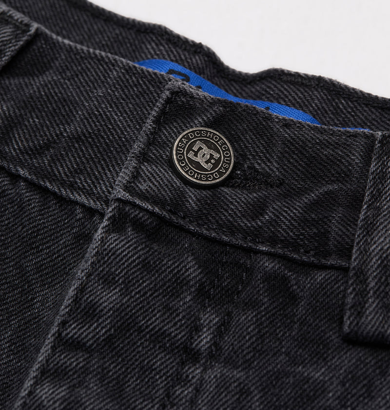 Close-up of the waistband on DC Shoes Men's Baggy Denim Snake Print Pant, featuring a metal button with DC Shoes logo and text, visible belt loops, and part of a blue fabric tag inside.