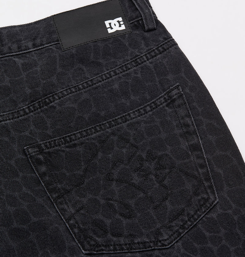 Close-up of the Men's Baggy Denim Snake Print Pant by DC Shoes, showing the black snake print pattern on the back pocket and a small black and white DC Shoes logo tag near the waistband.