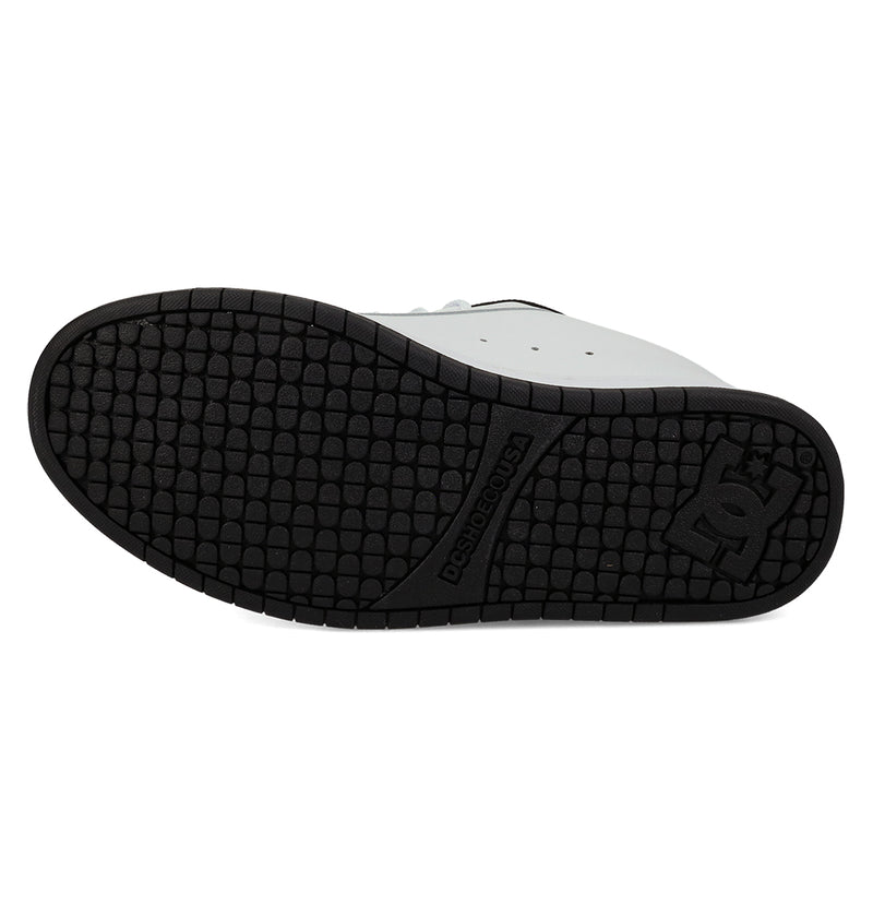 The image displays the sole of DC Shoes Men's Court Graffik Shoes, highlighting a black textured grip with the DC logo near the heel. The shoe features a bold, puffy silhouette in classic white and black.
