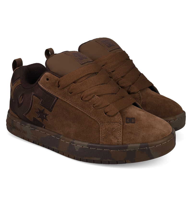 A pair of Men's Court Graffik SE Shoes by DC Shoes featuring brown suede, a puffy silhouette, wide laces, dark brown side logos, camouflage-patterned soles, low-top design, and reinforced stitching.