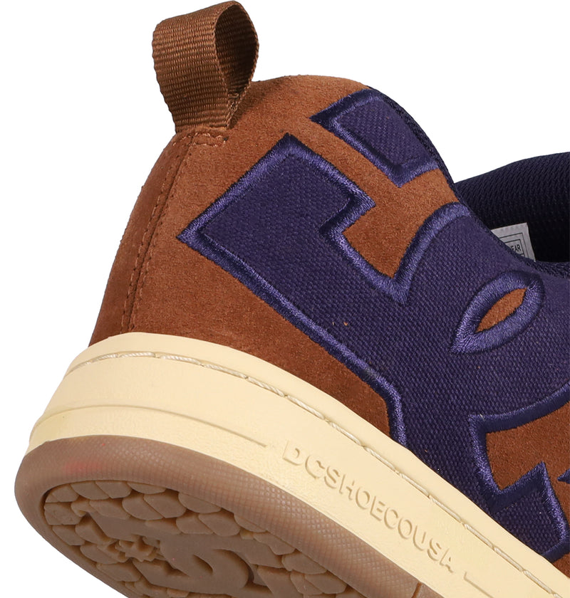 Close-up of the heel on DC Shoes Men's Court Graffik SE Shoes in brown and purple with a tan sole, featuring a large embroidered purple letter, brown pull tab, puffy silhouette, and DCSHOECOUSA embossed along the sole.