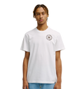 A young man with short, braided hair models the Men's DC Corpo Tee by DC Shoes—a relaxed fit, plain white t-shirt with a small black DC logo and circular emblem on the left chest—paired with light blue jeans against a white background.