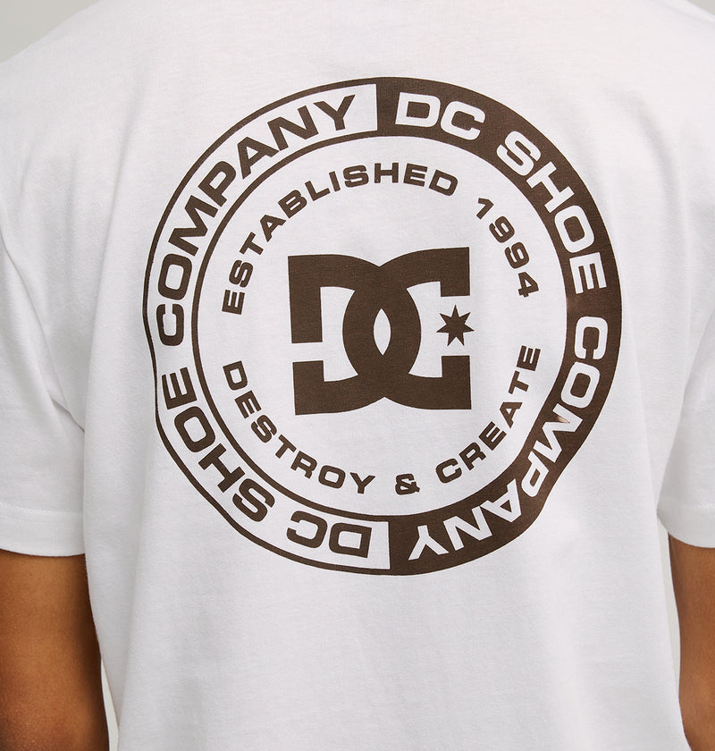 A person wears the Men's DC Corpo Tee by DC Shoes, a relaxed-fit skate tee featuring a large black circular DC Shoe Company logo on the back with "Established 1994" and "Destroy & Create" around the iconic graphic.