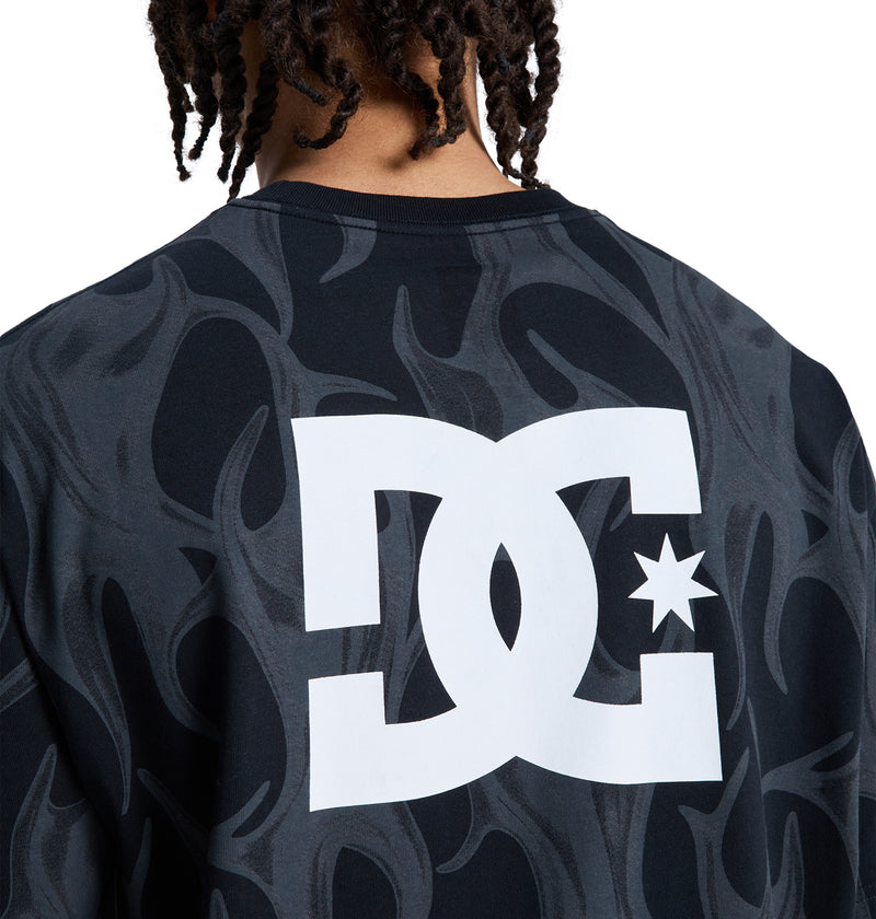 Seen from behind, a person with short dreadlocks wears a dark Reebok DC Liquid Fuego Hss shirt, featuring a large white logo and subtle flame patterns.