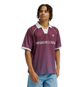 A young man models the Men's DC Soccer Top by DC Shoes, featuring maroon fabric with white trim, paired with light blue jeans against a plain white background for an athletic, casual look.