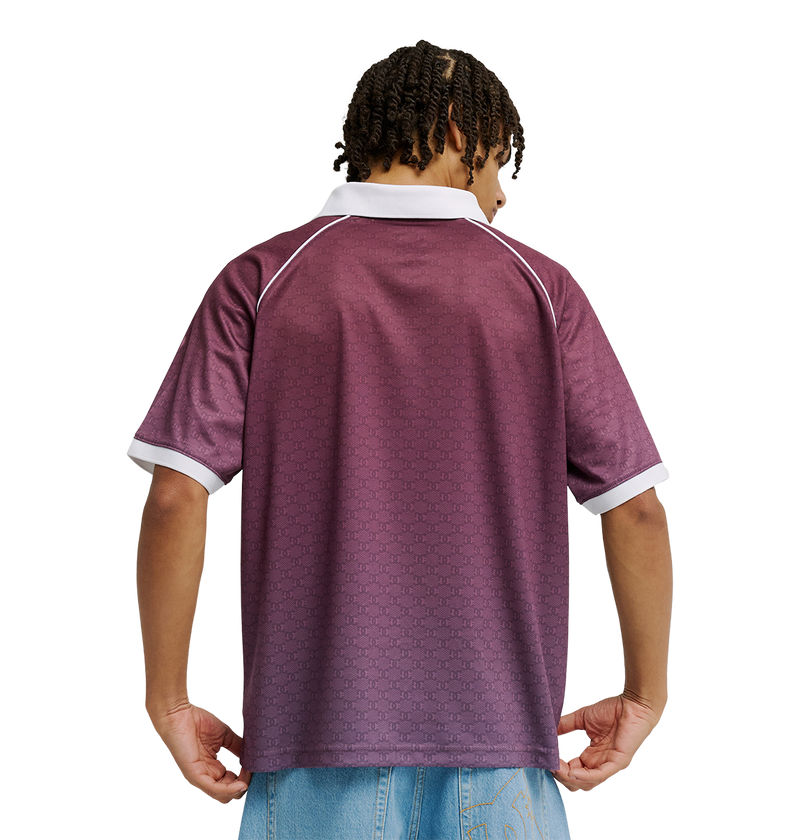 A person with short, curly hair is seen from the back wearing the Men's DC Soccer Top by DC Shoes—featuring a maroon color with white-trimmed collar and sleeves—styled with light blue jeans against a plain white background.