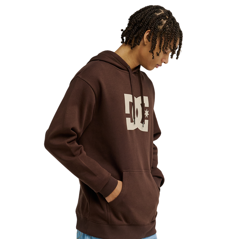 A person wears the men's DC Star Hoodie by DC Shoes—a brown pullover with large white DC graphics on the chest—standing with hands in the front pocket against a plain white background.