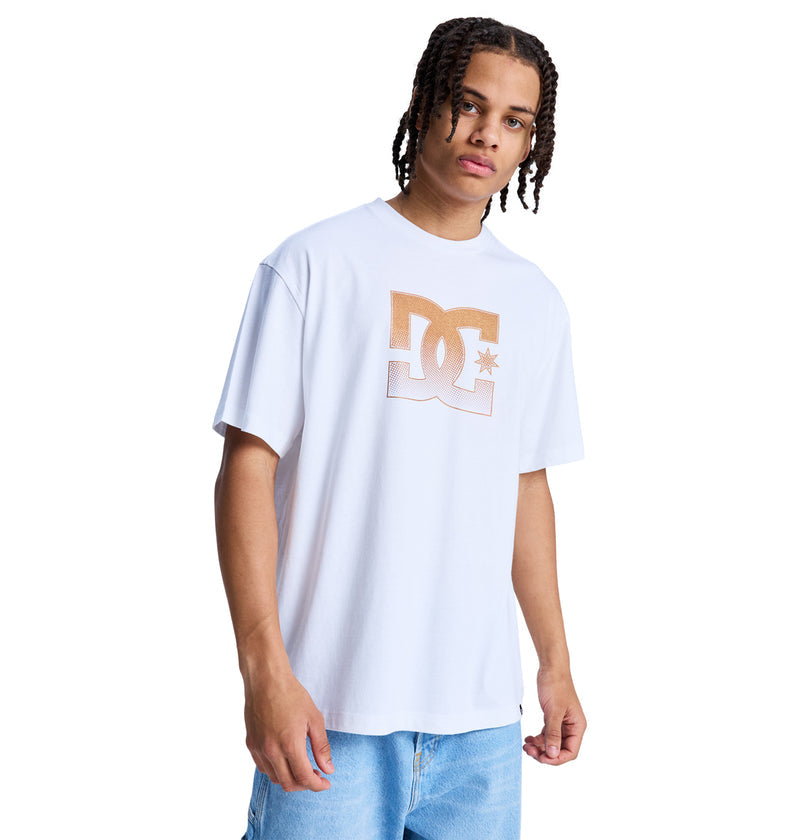 A young man with braided hair wears a white Reebok DC Star Oxidized Hss t-shirt with a bold front logo and blue denim shorts, standing against a plain white background.