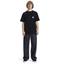 A person with curly hair wears the Men's DC Star Pocket Tee by DC Shoes in black, paired with relaxed fit dark jeans and black shoes, standing against a plain white background.