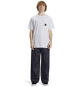 A person with curly hair wears the Men's DC Star Pocket Tee by DC Shoes—a relaxed fit white cotton skate shirt with a small logo—paired with wide dark jeans and black shoes, standing before a plain white background.