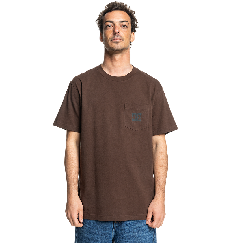 A man faces forward against a white background wearing the Men's DC Star Pocket Tee by DC Shoes—a relaxed fit brown cotton skate shirt with a chest pocket—paired with blue jeans.