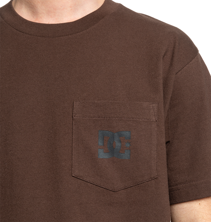 A person wears the Men's DC Star Pocket Tee by DC Shoes—a brown, relaxed-fit skate shirt with a small chest pocket and a dark gray DC logo. Only the upper torso is shown.