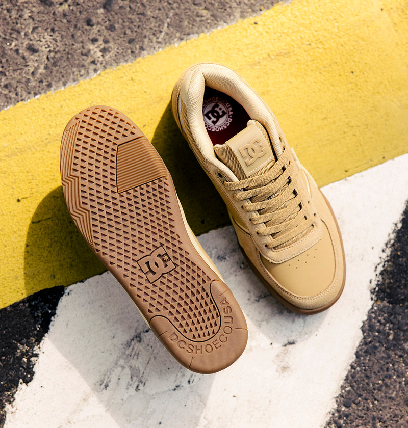 A pair of DC Shoes Men's Fractal S Shoes in tan, with one shoe upright and the other displaying the textured sole, are set on a street marked by yellow and white painted lines—an ideal scene to highlight their street-ready style and performance-driven comfort.
