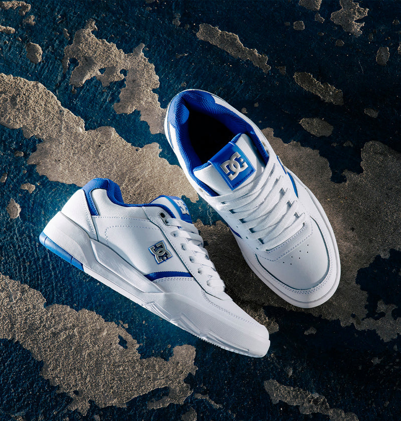 A pair of DC Shoes Men's Fractal S sneakers in white and blue, inspired by pro skater Will Marshall, displayed on a textured blue and gray surface—one shoe facing up and the other on its side—ideal for highlighting street-ready style.