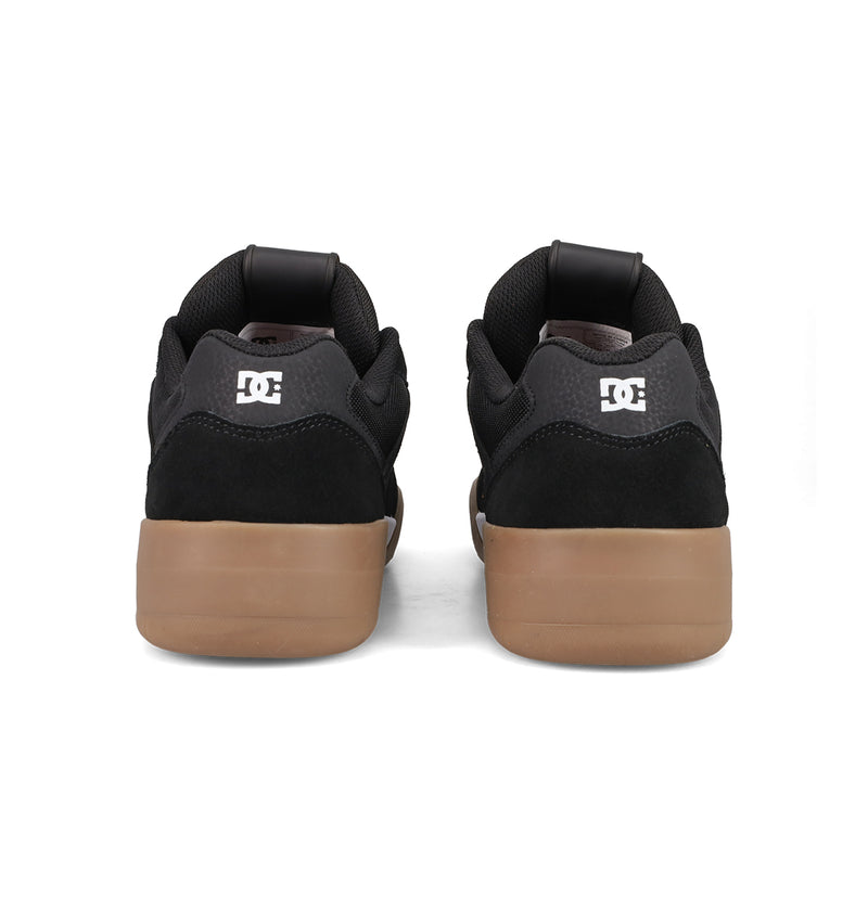 A pair of black Men's Fractal S Shoes by DC Shoes with brown rubber soles, shown from the back, featuring a white DC logo on the heel. These shoes offer street style and comfort against a plain white background.