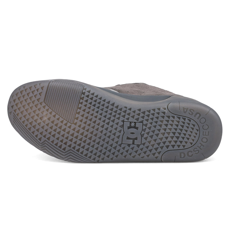 The image displays the sole of a grey DC Shoes Men's Fractal SE, featuring a textured triangular tread and the DC logo at the center. "DC SHOES" and "QUUSA" are molded into this street-inspired sneaker’s sole near the heel.