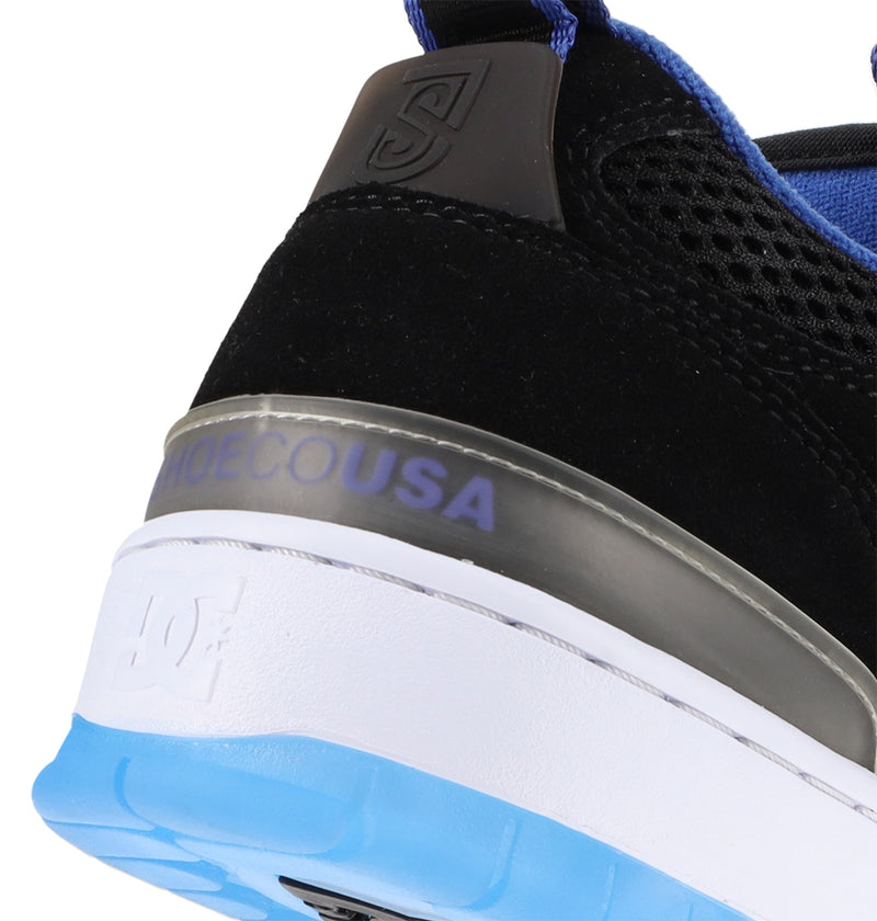 Close-up of the heel of the DC Shoes Men's JS-1 Shanahan Pro Skate Shoe with a black upper, blue inner lining, gray accent, and white and blue sole. SHOECOUSA appears above the DC Shoes logo on the heel.