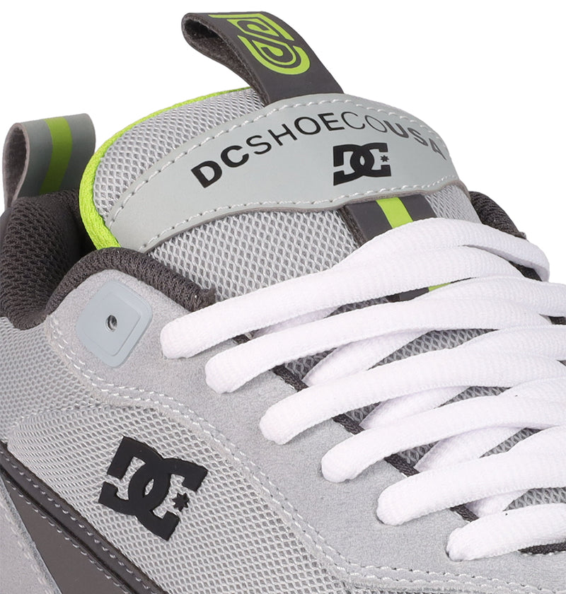 Close-up of the Men's JS 2 Shoes by DC Shoes in light gray, featuring white laces, mesh fabric, neon green accents, and brand logos on the tongue and side. This pro model is inspired by John Shanahan and DC heritage.