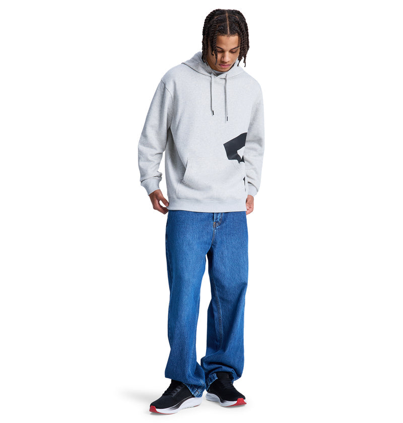A person models the Reebok Lanai Ph hoodie, featuring a black graphic on light gray, paired with loose blue jeans and black sneakers with white soles, standing against a plain white background.