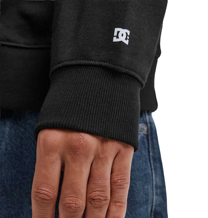A close-up of a person's hand resting on blue jeans, wearing a black Reebok Lorion Zh sweatshirt with a small white logo on the sleeve cuff.