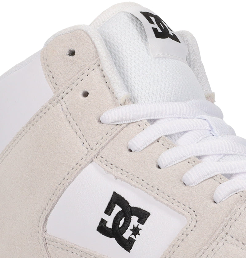 Close-up of the DC Shoes Manteca 4 Hi: a white sneaker featuring light gray suede accents, white laces, and the black DC Shoes logo embroidered on both the side and tongue.