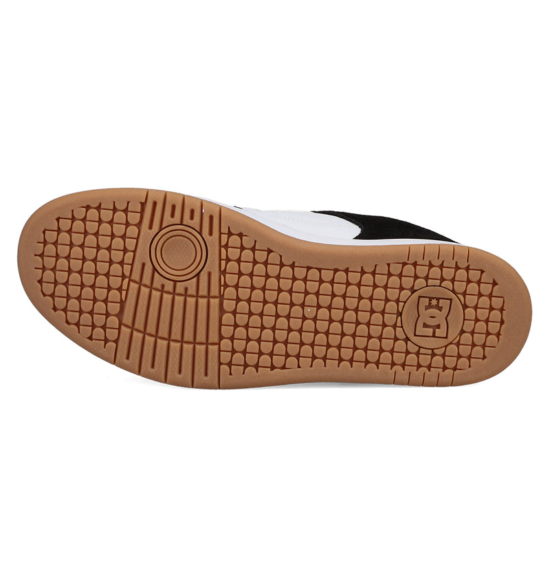 The image shows the gum-colored rubber sole of a Men's Manteca 4 shoe by DC Shoes, with multiple traction patterns and a logo near the heel. The partly visible upper in black and white adds to its classic style.