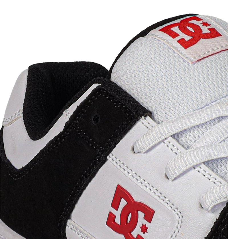 Close-up of a white and black Men's Manteca 4 Shoe by DC Shoes, showing the red logo on the side and tongue, white laces, padded black interior, and classic style.