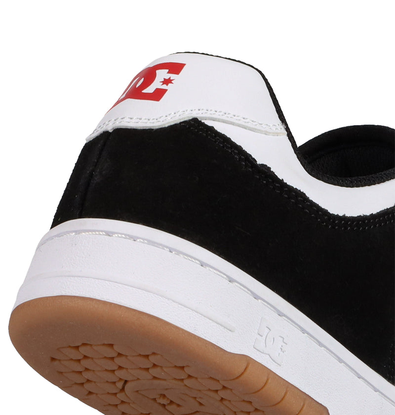 Close-up of the heel of a black and white Men's Manteca 4 shoe by DC Shoes, featuring a brown rubber sole, red DC Shoes logo on the white heel tab, and an embossed DC logo on the white midsole.