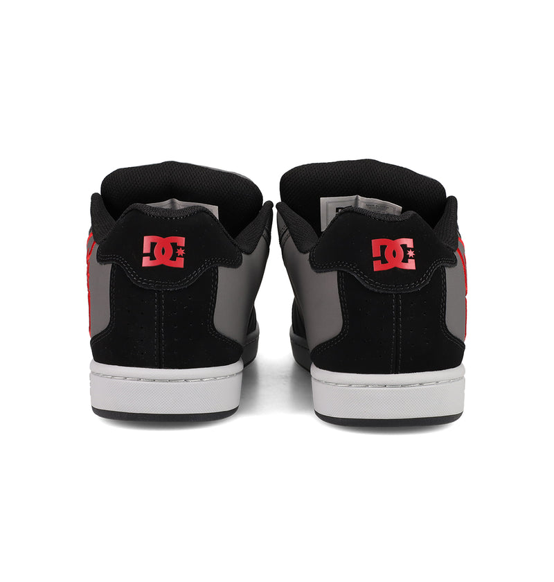 A pair of DC Shoes Men's Net Shoes shown from the back feature black, gray, and red colors with bold red DC branding on the heel. These puffy sneakers have white soles, black collars, and are made from durable fabrics.