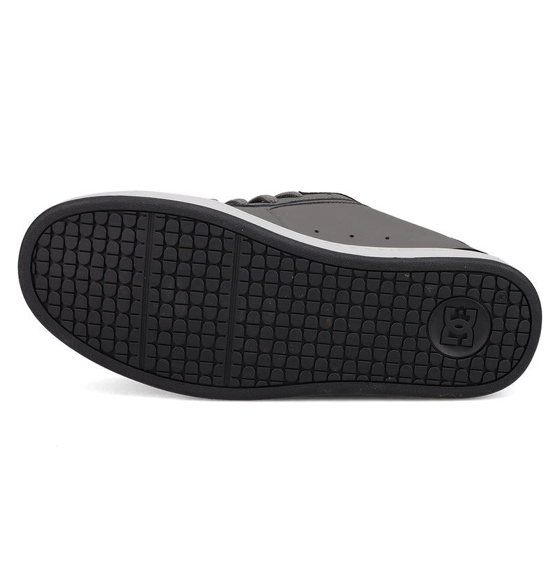 The image features the black rubber sole of DC Shoes Men's Net Shoes with a textured pattern and circular DC logo near the heel. A portion of the upper, made from durable dark-colored fabric, is also partly visible.