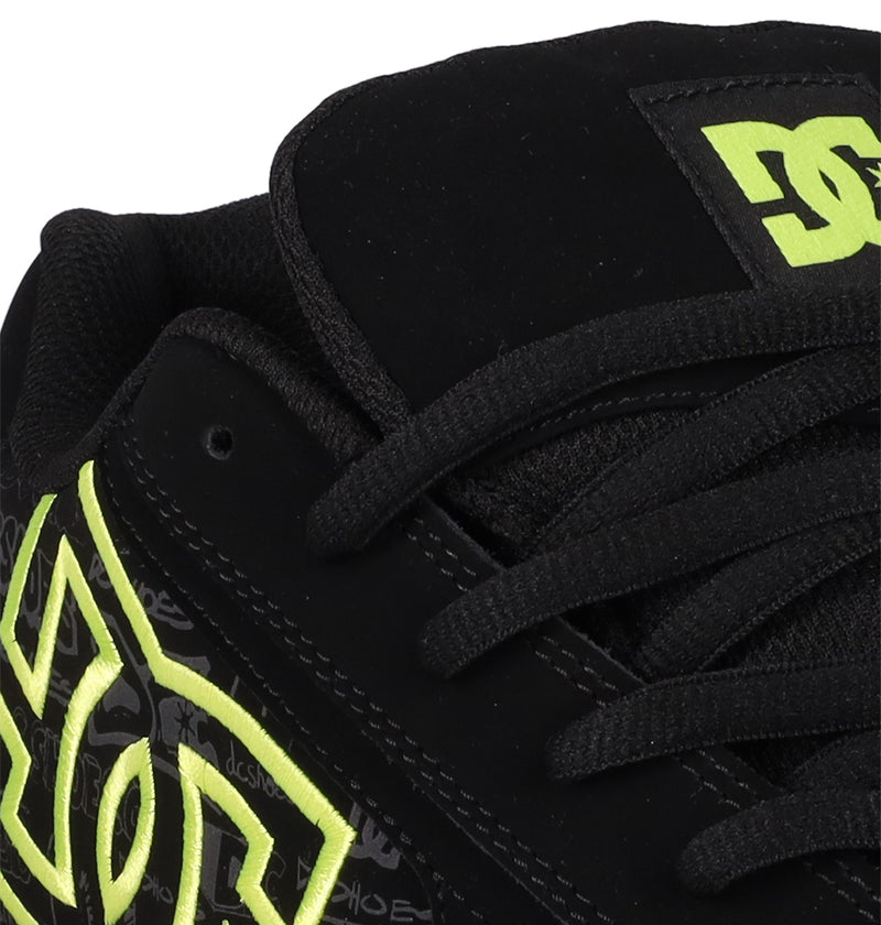 Close-up of Men's Net Shoes by DC Shoes, featuring a black design with neon yellow DC branding on the side and tongue, black laces, padded collar, and durable fabric construction.
