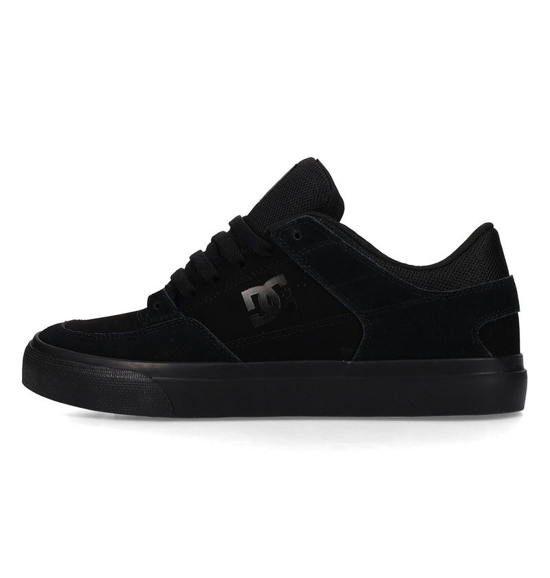 A black low-top skate shoe with a suede and mesh upper, black laces, a rubber sole, and the DC Shoes logo on the side.